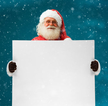 Real Santa Claus holding white blank sign for your text / Merry Christmas & New Year's Eve concept / Closeup on blurred blue background.
