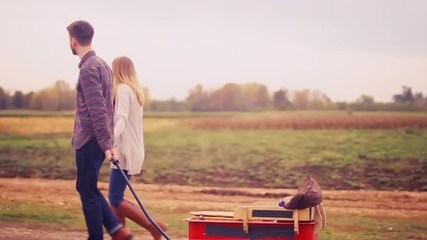 A couple walking and holding hands while pulling their baby in a wagon at a pumpkin patch