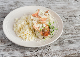 Baked fish with lemon and herbs and cous cous on a white plate, on bright wooden surface. Healthy food