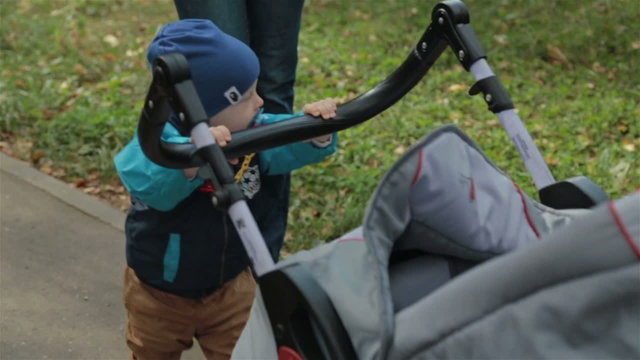 Small child toddler boy pushing a carriage in the park, slowmotion