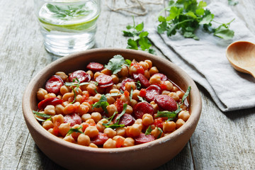 Chickpeas with chorizo in a clay bowl on the table close-up 