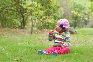 Little girl sits on a meadow and eats candy.