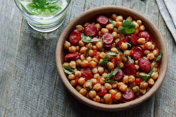 Chickpeas with chorizo in a clay bowl on the table close-up 