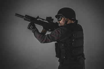 airsoft player with gun, helmet and bulletproof vest on gray bac