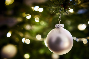 Silberne Weihnachtskugel vor grünem Tannenbaum-Bokeh.