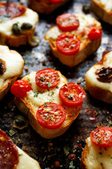 Crostini with cheese, tomatoes and herbs on a dark background