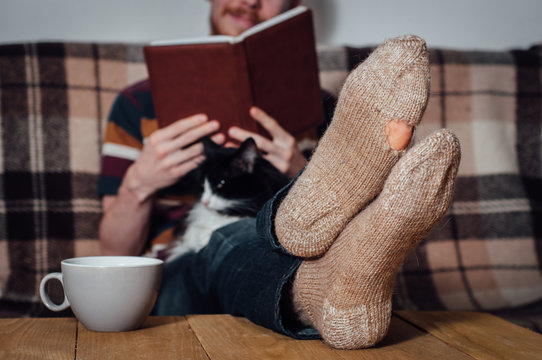 Young man reading book on coach with cat in holey socks