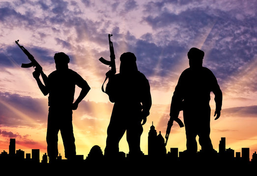 Silhouette of men with rifle standing in front of city during sunset