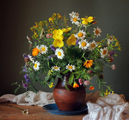 Still life with a summer bouquet of wild flowers in a clay jug.