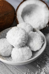 Candies in coconut flakes and fresh coconut on color wooden background