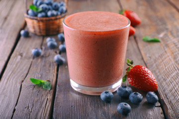 A glass of fresh cold smoothie with berries, on wooden background