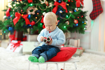 Fototapeta na wymiar Funny baby sitting on sledge and Christmas tree and fireplace on background