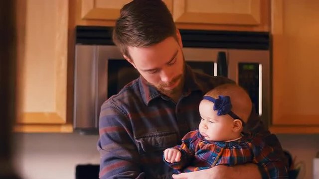 A young father holding and talking to his baby in the kitchen