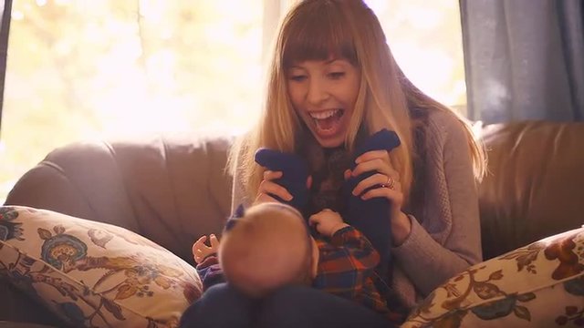 A mother playing with her baby at home on the couch and kissing her feet