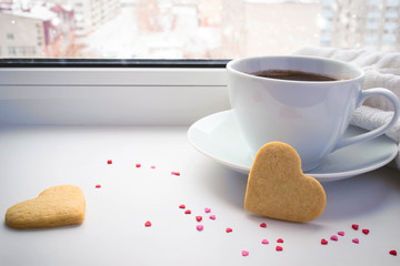 Cup of coffee and cookies valentines on background of a winter w