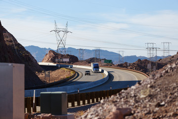 Asphalt road in the bend with truck and two cars on high voltage lines, rocks, cliffs and blue sky background