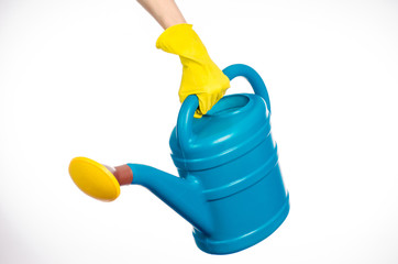 Caring for the plants and the garden theme: the human hand in yellow rubber gloves holding a large blue plastic watering can isolated on white background in studio