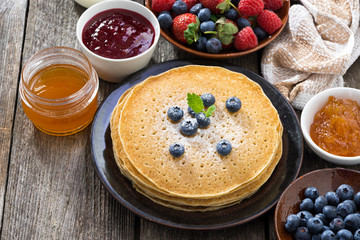 crepes, fresh berries and jams on wooden table, top view