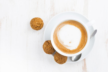 cup of cappuccino and flavored cookies on white wooden table