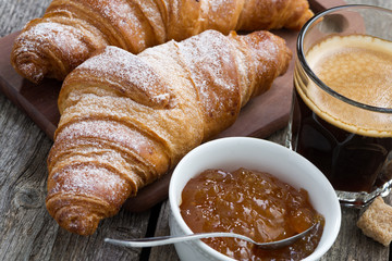 fresh croissants, coffee and orange jam on a wooden background