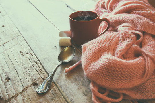 selective focus photo of pink cozy knitted scarf with to cup of coffee on a wooden table. workspace or coffee break. retro filtered
