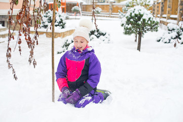 Little girl in colorful suit play in snow in back yard