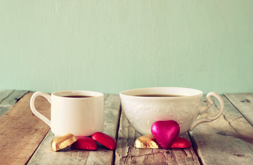 image of two red heart shape chocolates and couple cups of coffee on wooden table. valentine's day celebration concept
