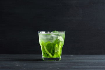 Green cocktail with kiwi slices on black wooden background