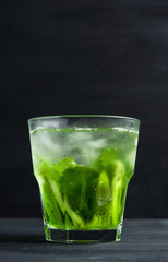 Green cocktail with kiwi slices on black wooden background