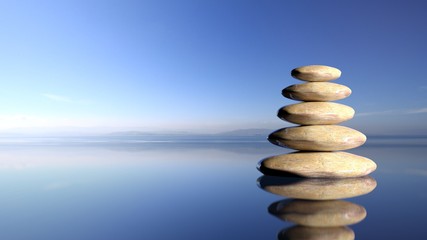 Zen stones stack from large to small  in water with blue sky and peaceful landscape background.