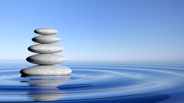 Zen stones stack from large to small  in water with circular waves and blue sky.