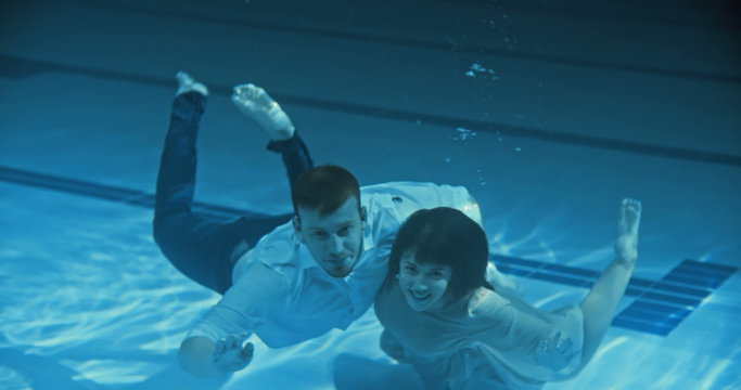 Smiling couple swimming underwater towards the camera and waving