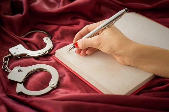 Handcuffs on red satin and woman writing in notebook