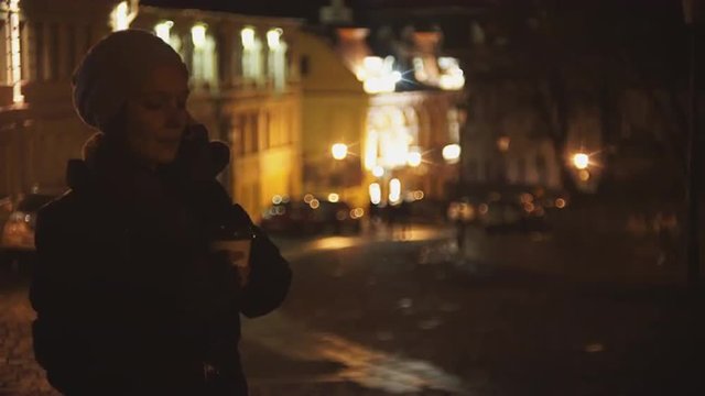 Woman on the street of the evening drinking coffee and talking on the phone