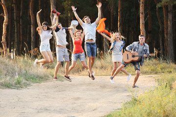 Happy smiling friends with musical instruments jumping in the forest outdoors