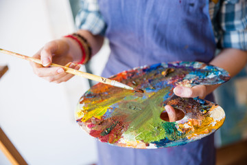 Palette with mixed paints holded by hands of woman artist