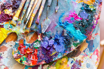 Closeup of art palette with colorful mixed paints and paintbrushed - obrazy, fototapety, plakaty