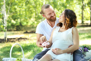 Handsome man and his lovely pregnant wife with baby booties  in the park