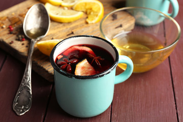 Mulled wine in a mug with citruses on wooden background, close up