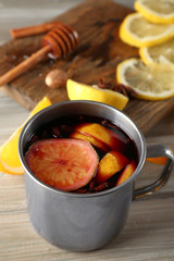 Mulled wine in a mug with citruses on wooden background, close up