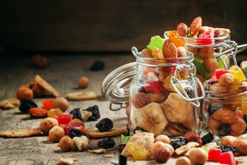 Nuts and dried fruits in glass jars on the old wooden table, sel