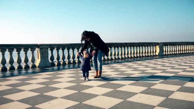 Sweet beautiful moment. Mother teaching her baby first steps in a terrace by the sea.