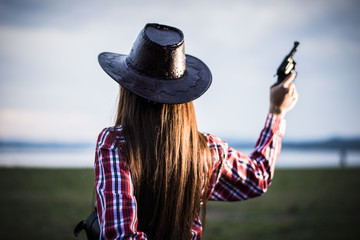 Portrait of a cowgirl in a hat holding gun