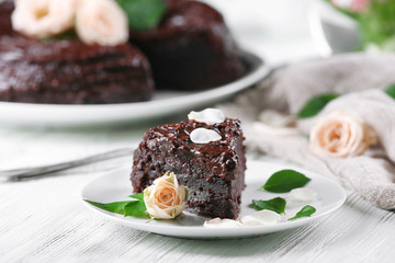 Piece of chocolate cake decorated with flowers on white wooden table