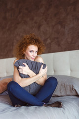 Obraz premium Flirty attractive curly woman sitting on bed hugging pillow