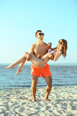 A guy holding a girl in the arms, at the beach, outdoors