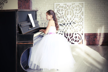 Naklejka premium Attractive little princess girl plays piano