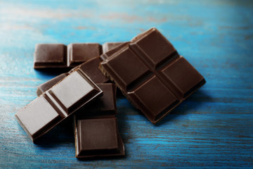 Black chocolate pieces on color wooden background