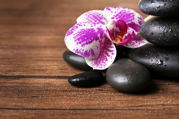 Fototapeta na wymiar Black pebbles with orchid on wooden background
