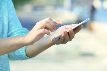 Female hands holding a mobile phone outdoors, on blurred background